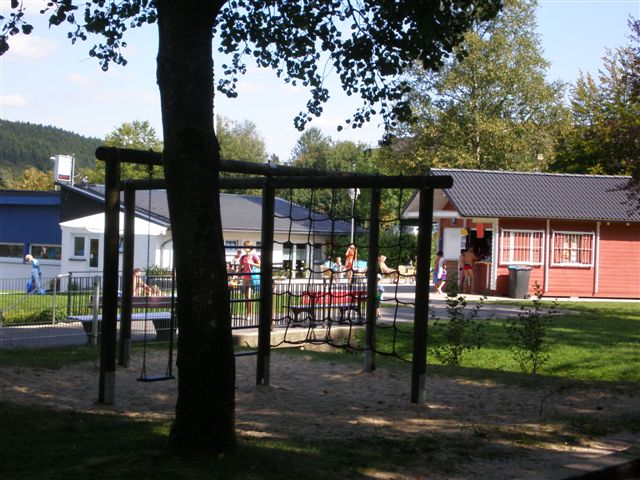 Ein Klettergerüst mit einem Sandkasten und dem Kiosk im Hintergrund. 