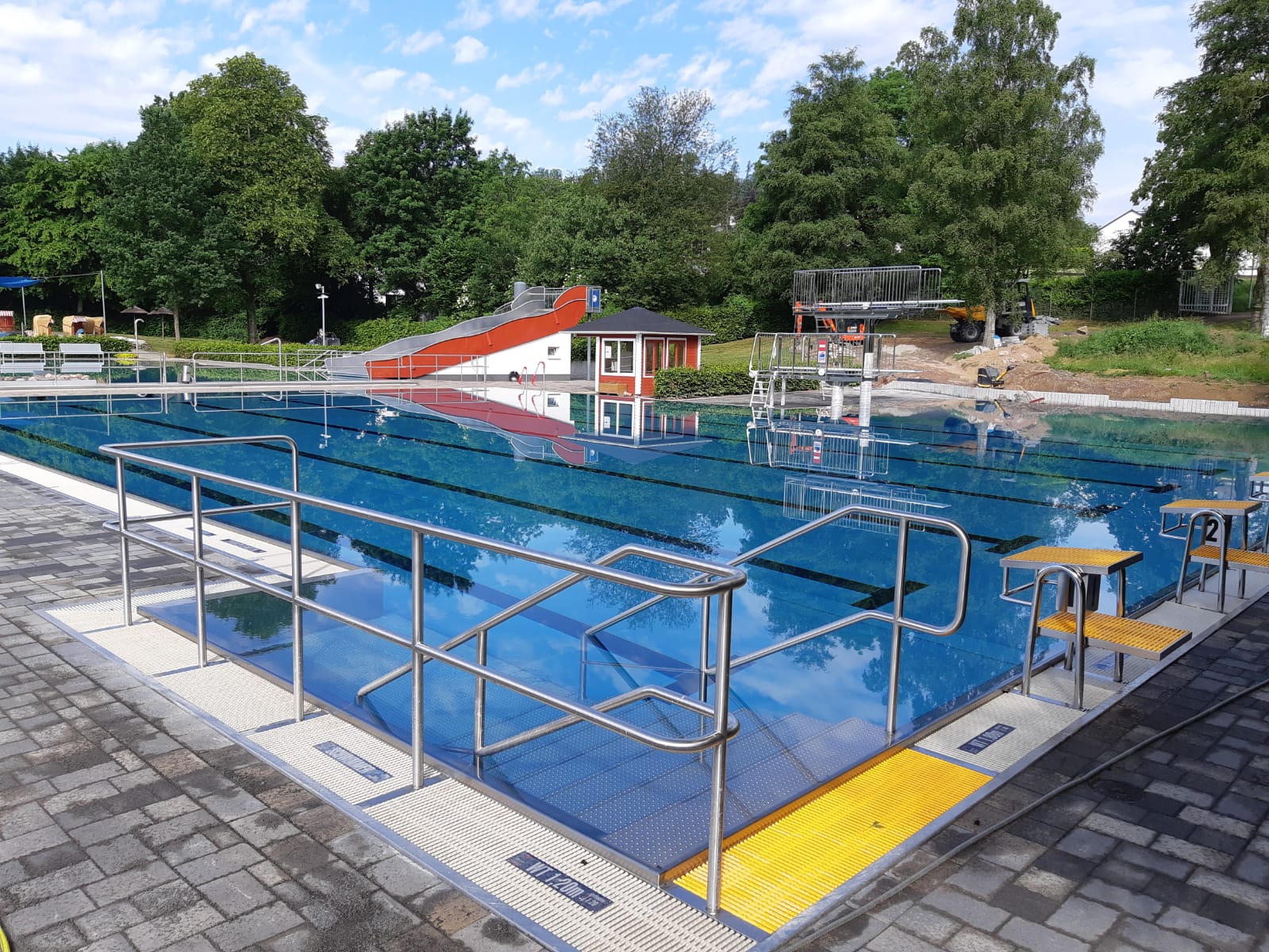 Mit Wasser gefülltes Sportbecken des Freibads in Herscheid mit Wiese und Bäumen im Hintergrund